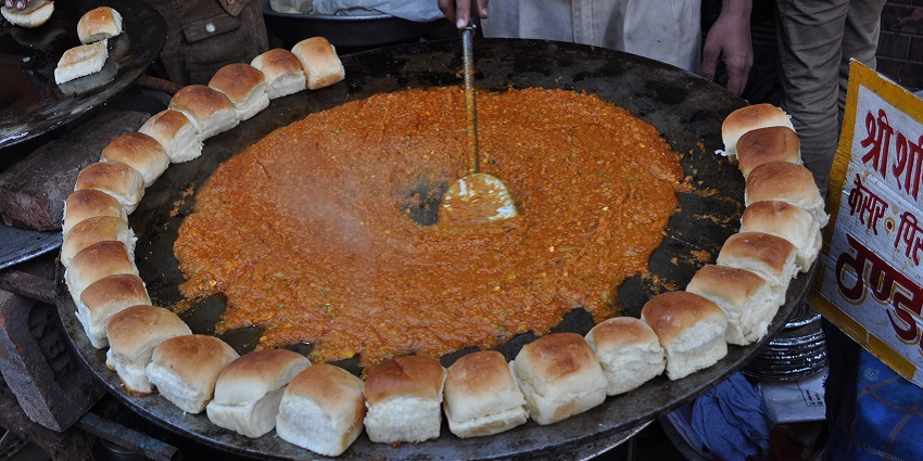 A person preparing bhaji and roasting pavs in butter on a big tava next to a small tava.