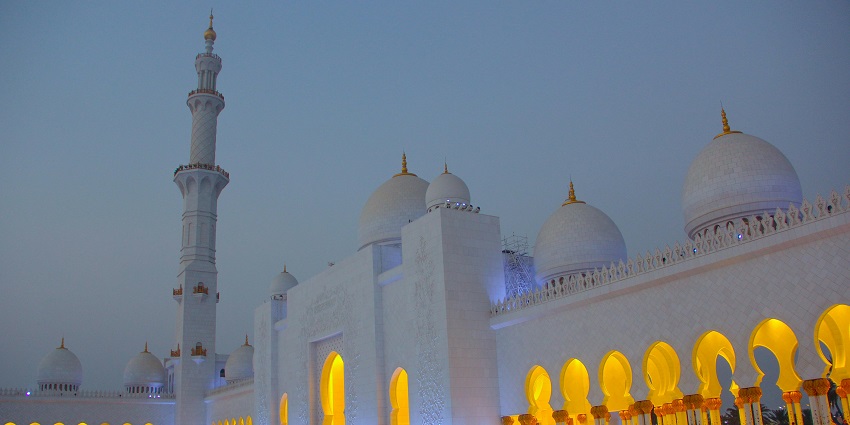 A picture of a mosque taken during nighttime with the worship house being illuminated with various lights