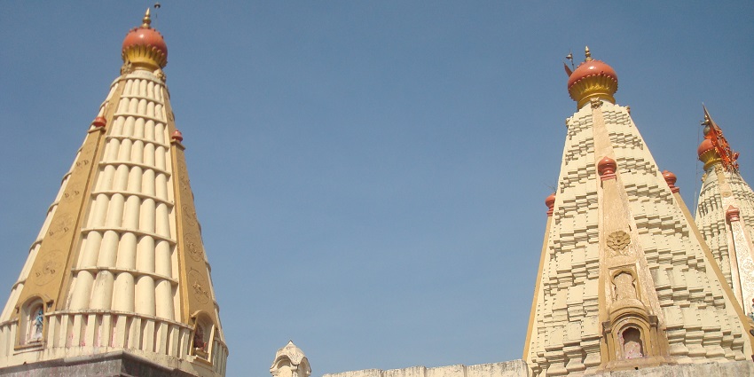 Vibrant temple complex with pink walls, intricate carvings, and devotees in a lively courtyard