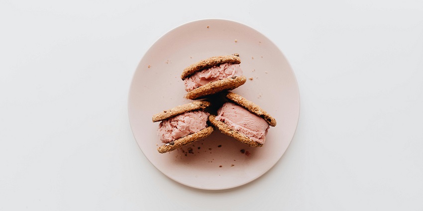Three chocolate chip cookie sandwiches with ice cream served on a plate together