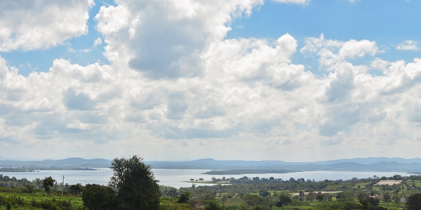 A wide, open landscape with a large lake surrounded by green vegetation under a sky
