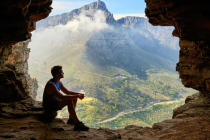 The image shows a man sitting inside a large cave in Maharashtra looking out.