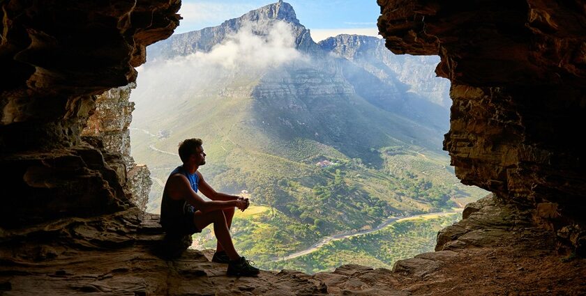 The image shows a man sitting inside a large cave in Maharashtra looking out.