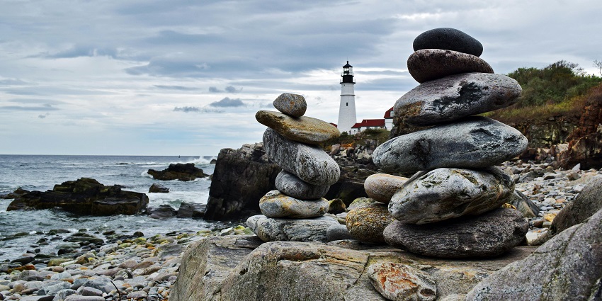 A lighthouse visible through the huge rocky cliffs on an island with clear skies.