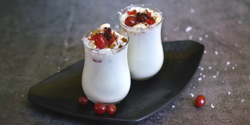 Two lassi glasses topped with mawa, grated coconut, cherry, and dry fruits on a tray.