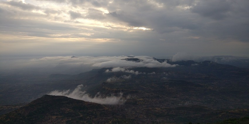 A vibrant sunrise over a foggy landscape, seen from Kalsubai Peak with a golden sky and misty valleys.