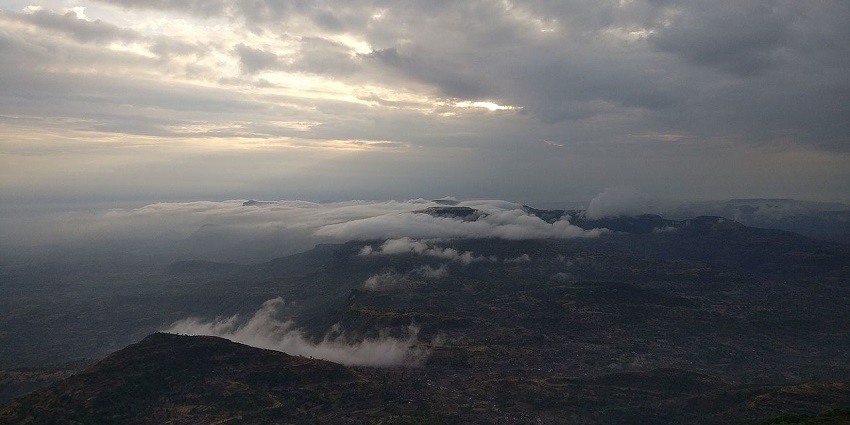 An aerial view of Kalsubai Peak with white clouds, a popular destination near Thanale Caves.