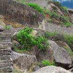 The ancient Kamandurg Fort with a tall mountain backdrop, surrounded by greenery.