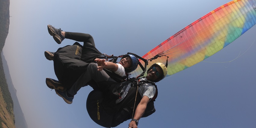 A picture of a trained paraglider paragliding with a tourist over the lush greenery of Kamshet