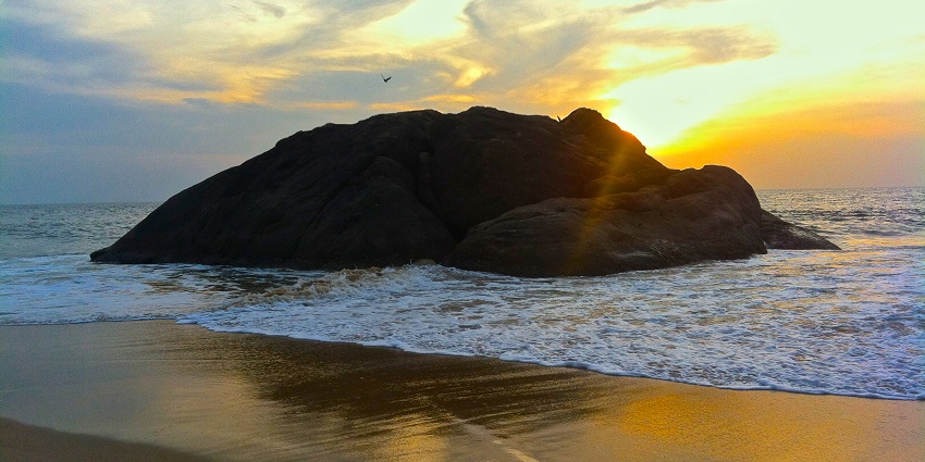 Water, sand, and large rocks at Kaup Beach, a scenic tourist attraction in Udupi.