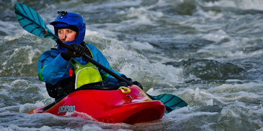 Professional Kayaker paddling through moderate levels of water currents in a red kayak.