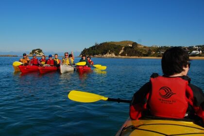 A group of people kayaking in Abel Tasman National Park's crystal-clear water amid hills.