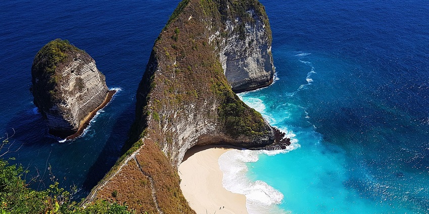 Coastal landscape of Kelingking Beach with cliffs, clear blue sea, and rocky shoreline.