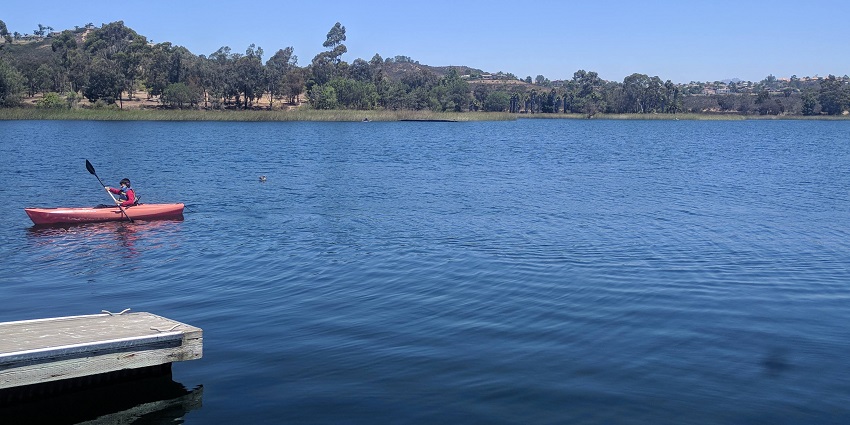 A person kayaking on the waters of Khadakwasla Lake, surrounded by a green landscape