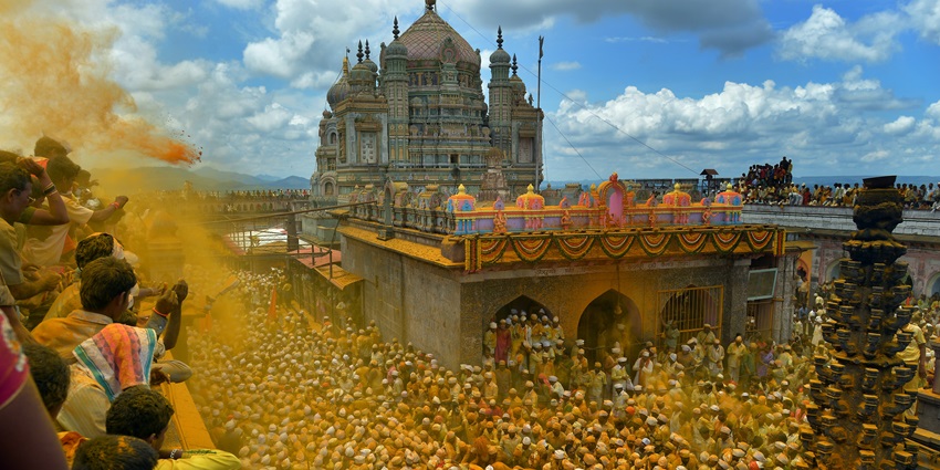A picture of Khandoba Temple atop a hill, surrounded by devotees and yellow turmeric powder