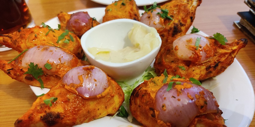 A plate of golden brown tandoori momo garnished with coriander and sliced onions