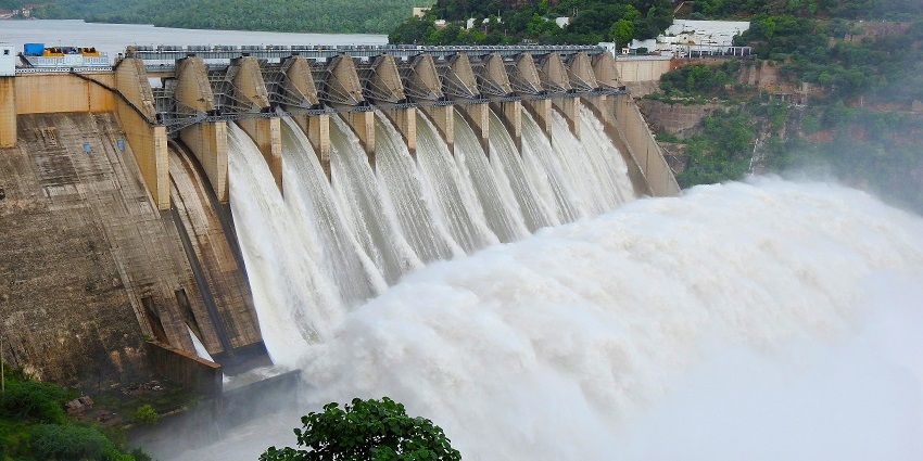 A large dam spanning a river, surrounded by lush greenery and hills under a clear sky