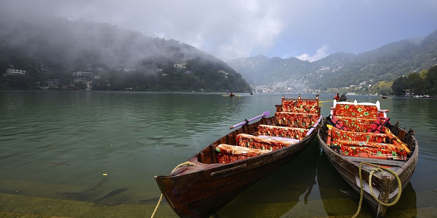 Two boats docked near the bank of a lake surrounded by lush and foggy hills
