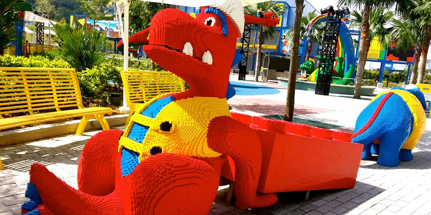 Image of a park outdoor with colourful decorations, rides and Lego dinosaur made