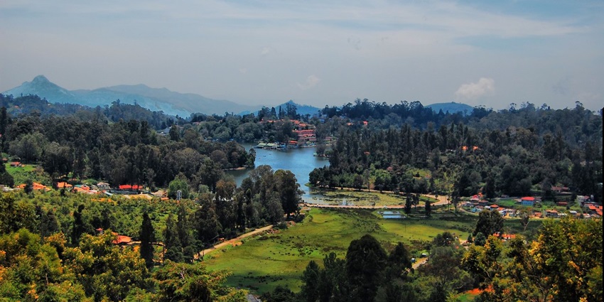 A majestic view of a serene lake surrounded by lush green forest near Erode