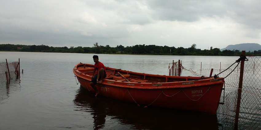 Image of a man sitting on a boat around the lake surrounded by lush greenery