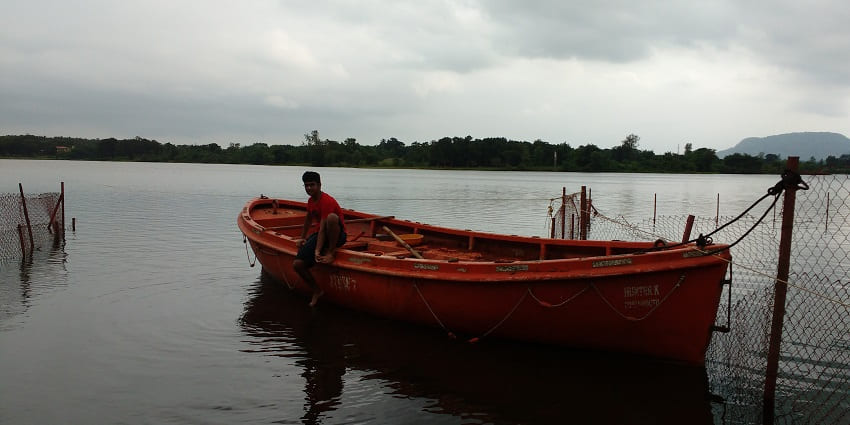 A man sitting on a chained boat in the river flowing through Kolad, surrounded by hills