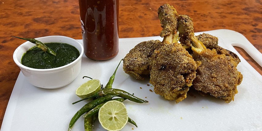 Fried Chicken served on a plate accompanied by green dip, lemons, fried chilli and a drink