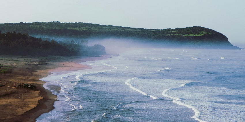 Misty view of the beach with brown and grey rocks in the foreground