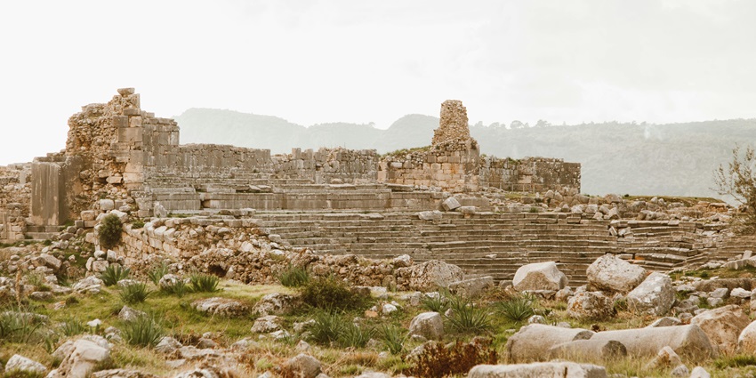 An image of ancient stone temple ruins surrounded by greenery, with worn pillars.