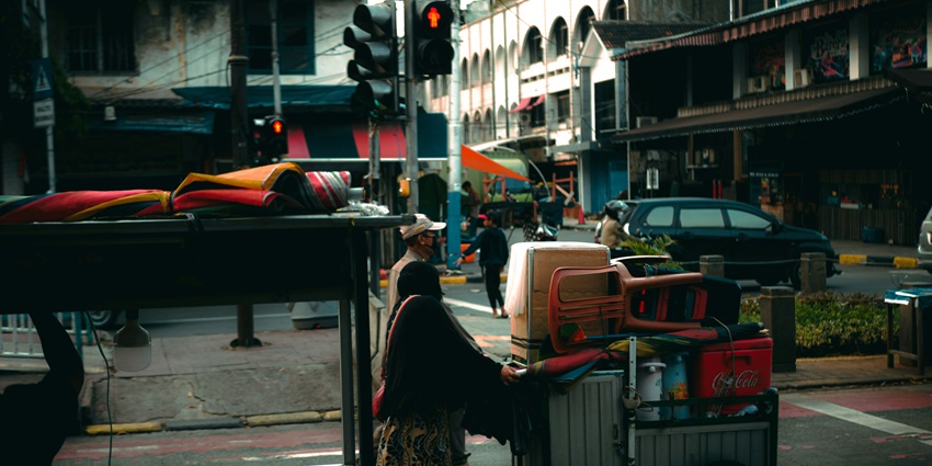 An image of a woman pushing a cart filled with luggage of different sizes in Kota Tua.