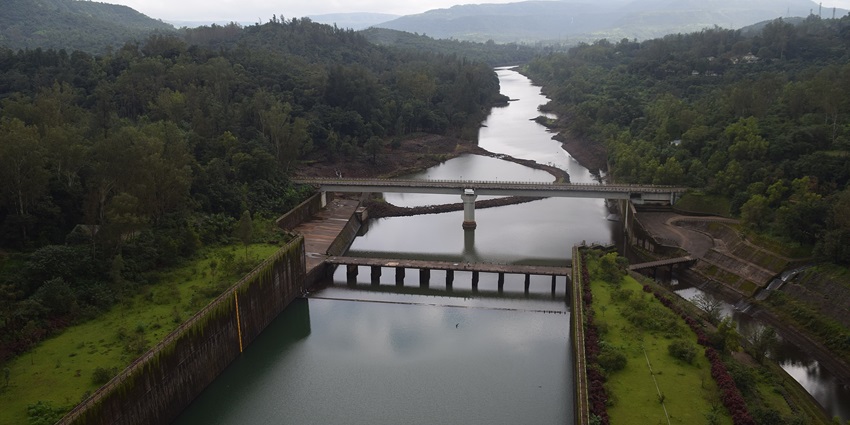 A scenic view of Koyna Dam surrounded by lush green hills and water