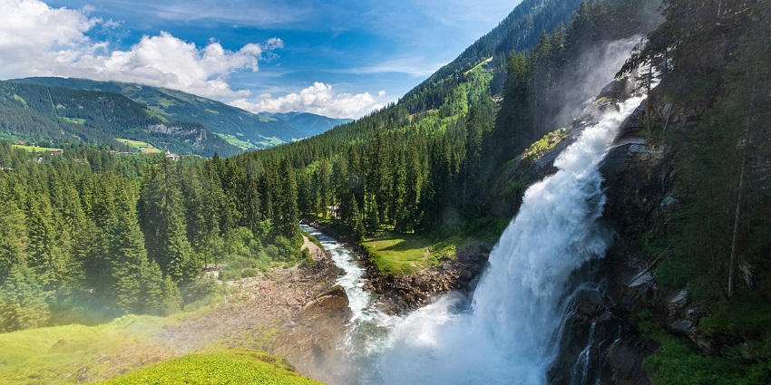 Waterfall in a forest setting, surrounded by mountains and greenery.