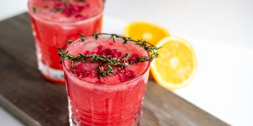 A clear glasses with red drink, garnished with a lemon slice on the rim.