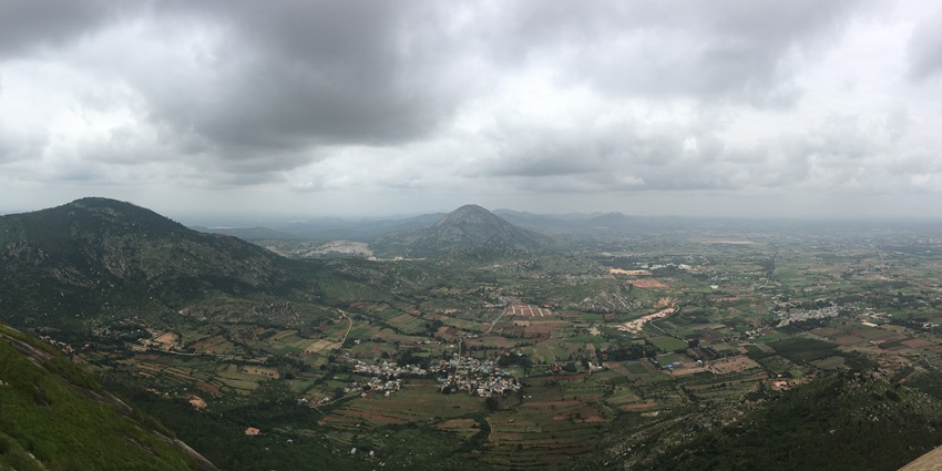 Panoramic view from Nandi Hills showing lush valleys, winding roads, and distant plains at sunrise.