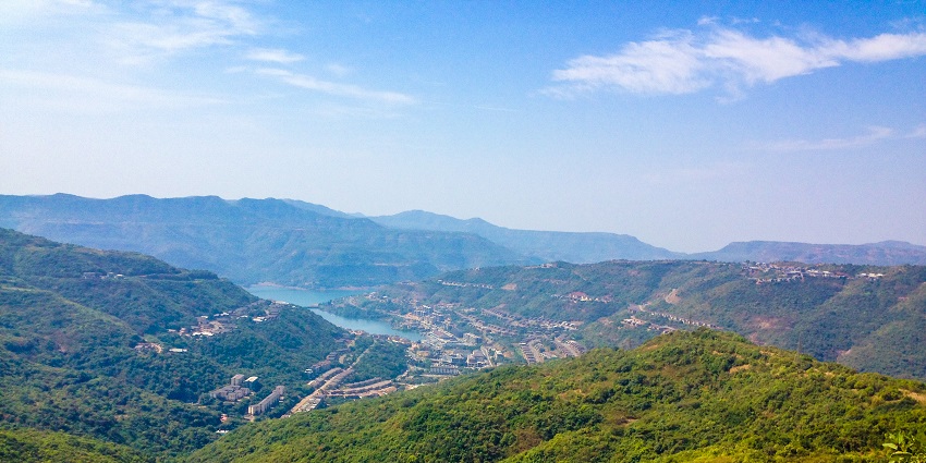 The peaceful lake in Lavasa, surrounded by green mountains under a partly cloudy sky.