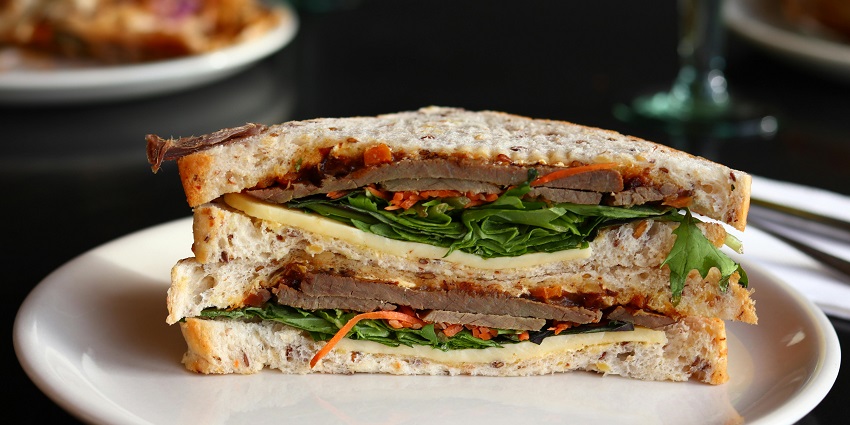 A half-cut sandwich filled with layers of lettuce, bell pepper, and cheese slice