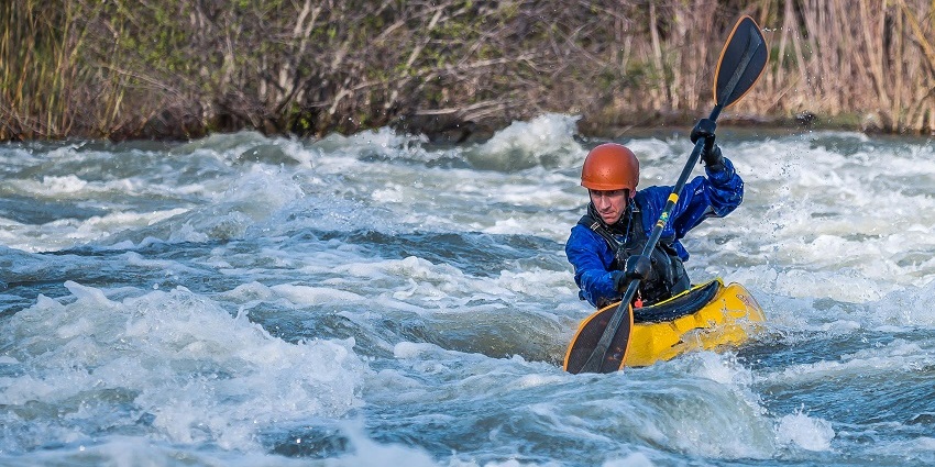 A man kayaking in Kolad, paddling a yellow kayak through fast-flowing river