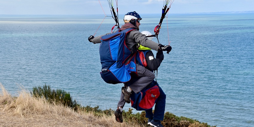 Tandem paragliders on the edge of a hill, preparing to take off slightly in mid-air
