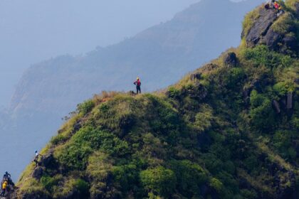 A tall, rocky pinnacle rises above lush green hills under a clear blue sky in Maharashtra.