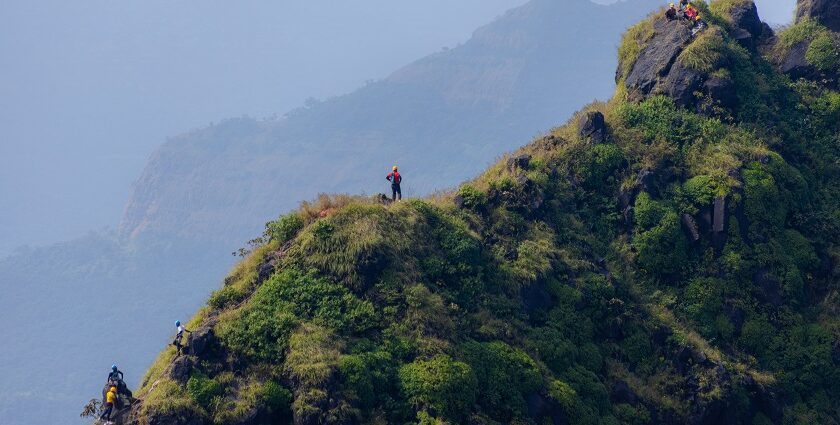 A tall, rocky pinnacle rises above lush green hills under a clear blue sky in Maharashtra.