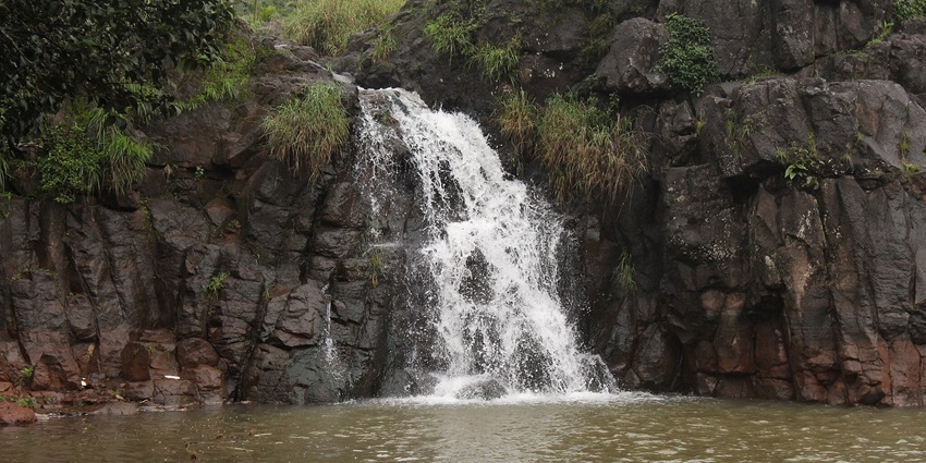 Scenic view of Lingmala Waterfall, with water cascading down dense vegetation and green hills.