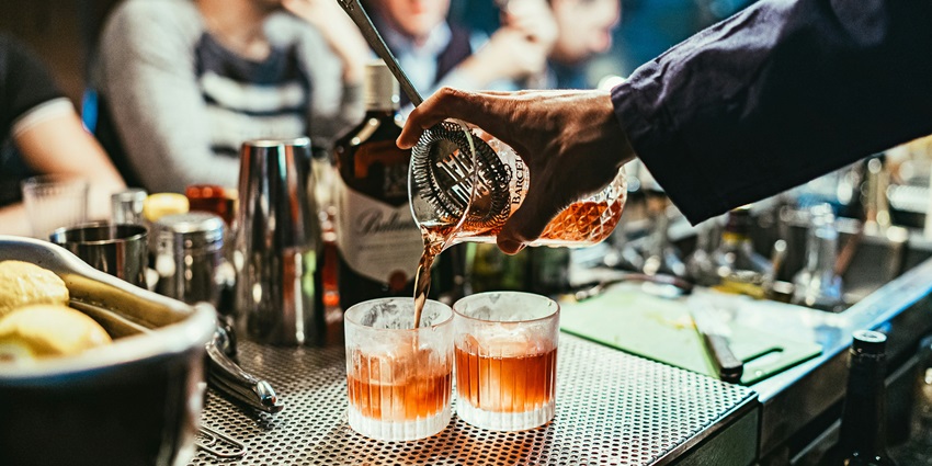 Person pouring a drink from a bottle into a glass at a warmly lit bar setting