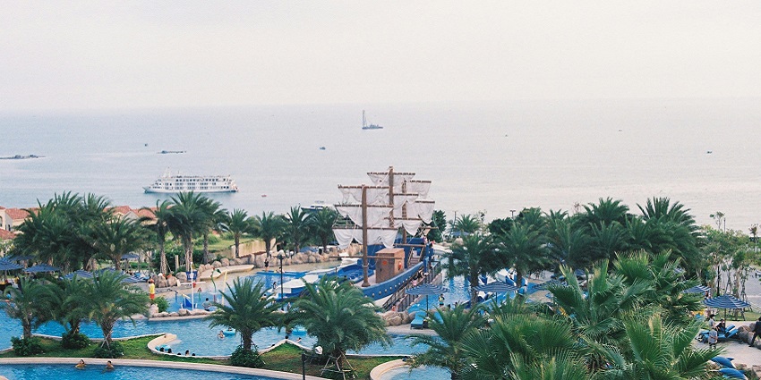 Recreational area featuring swimming pools, palm trees, and a ship, perfect for relaxation and fun.