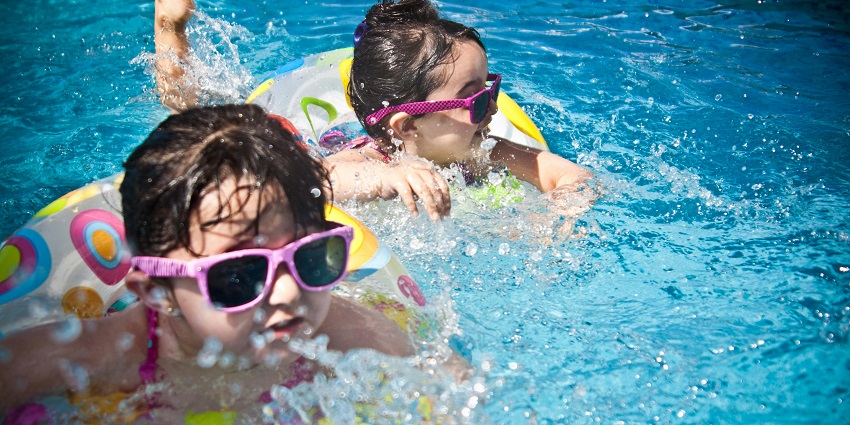 Two girls enjoying a swim together in a sunny pool during the daytime.