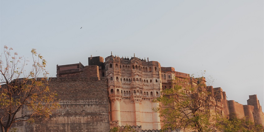 An outer view of an old fort with thick walls is surrounded by lush green trees