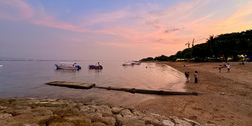 A serene sunrise over Sanur Beach in Bali, with the golden sun rising above the horizon