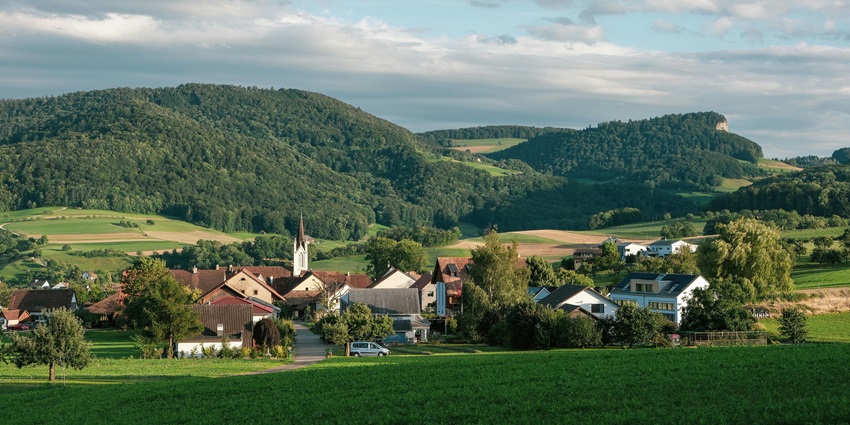 Green countryside village with houses and fields under a clear blue sky.
