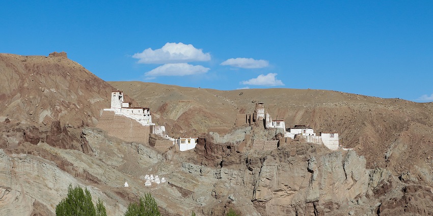Image of Basgo Monastery, Ladakh surrounded by brown rocky mountains under white clouds and blue sky