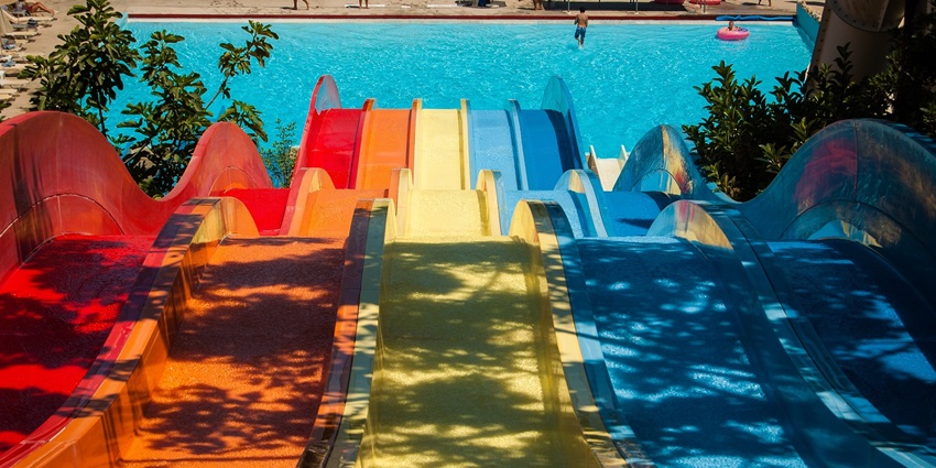 A vibrant water slide at a sunlit water park, surrounded by green trees and clear blue skies.