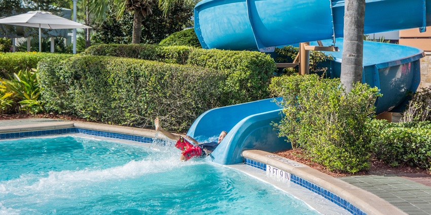 A child slides down a colorful water slide into a bright blue pool on a sunny day